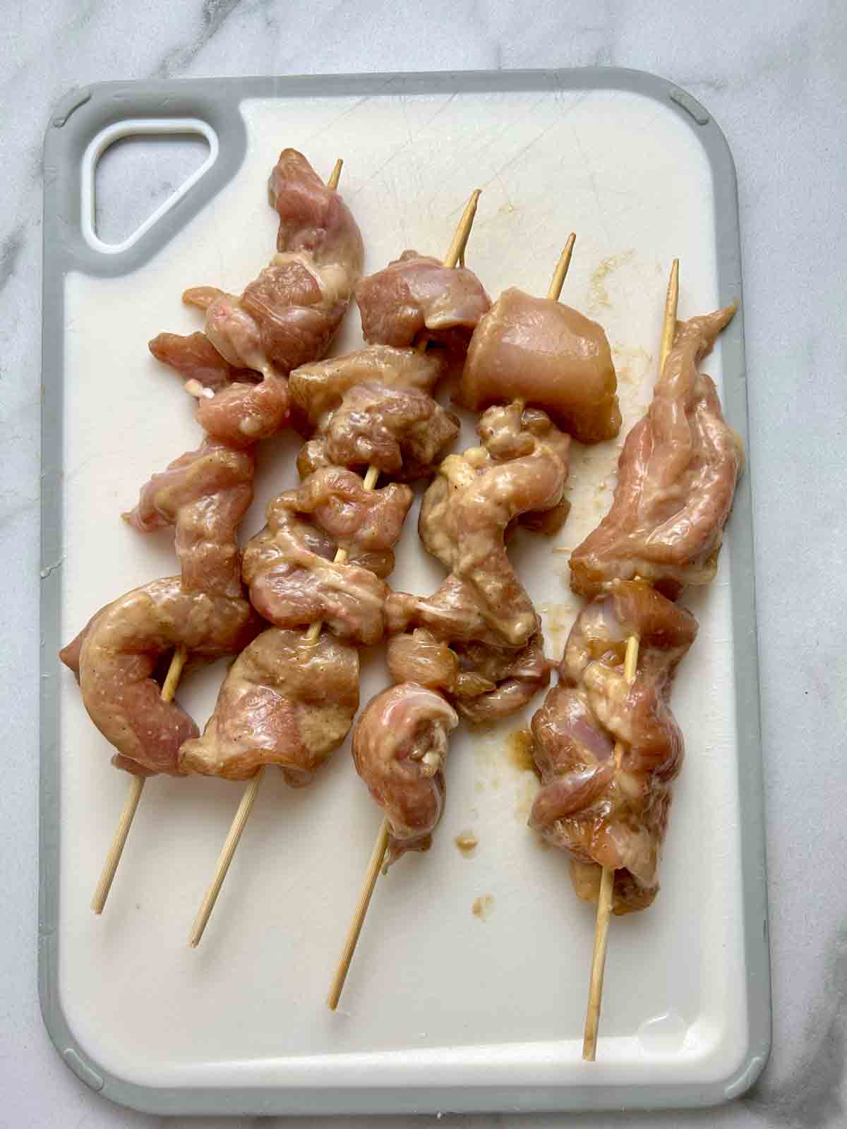 four skewers of marinated chicken on cutting board.