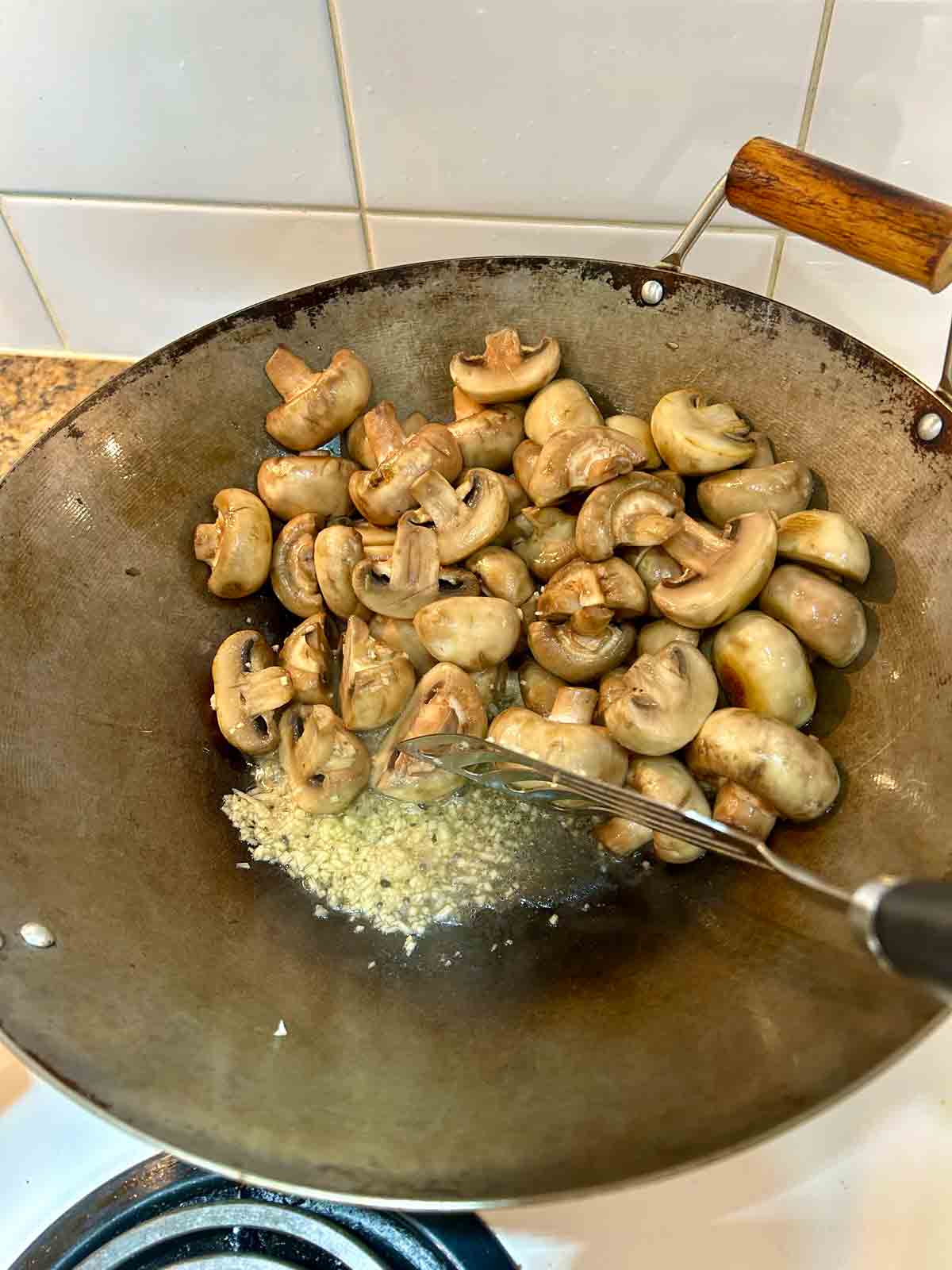 garlic cooking in oil next to mushrooms.