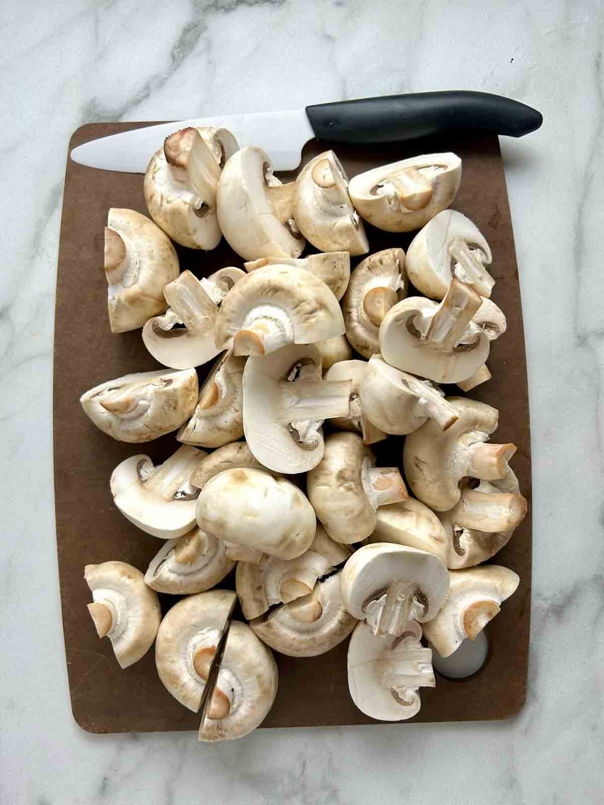 halved mushrooms on wooden cutting board with knife above it.