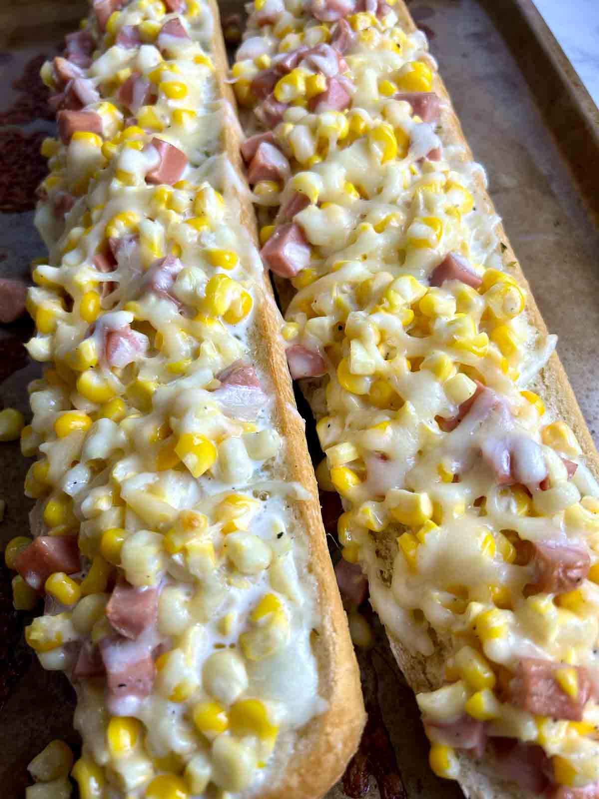 close up showing ham, corn, and cheese toppings on garlic bread.