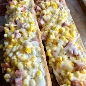 close up showing ham, corn, and cheese toppings on garlic bread.