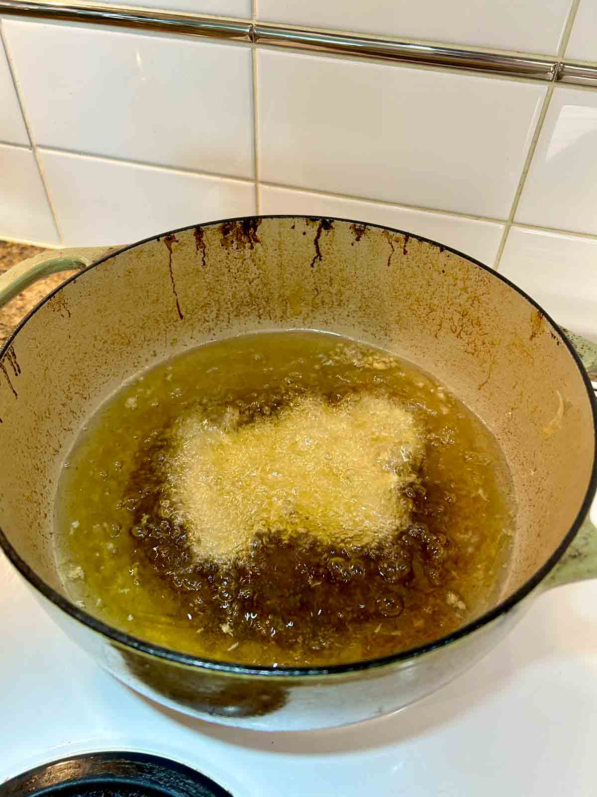 breaded chicken being fried in hot oil in Dutch oven.