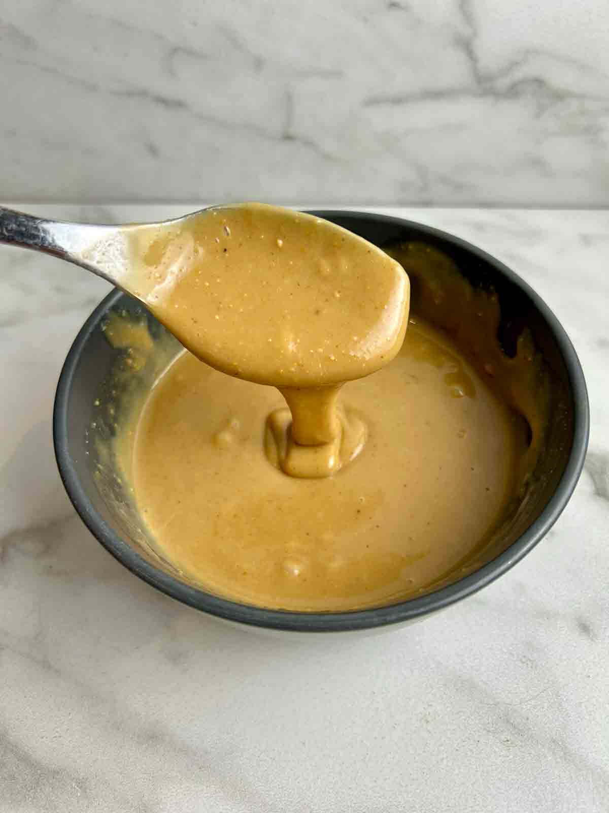 peanut butter sauce drizzling back into bowl from spoon.