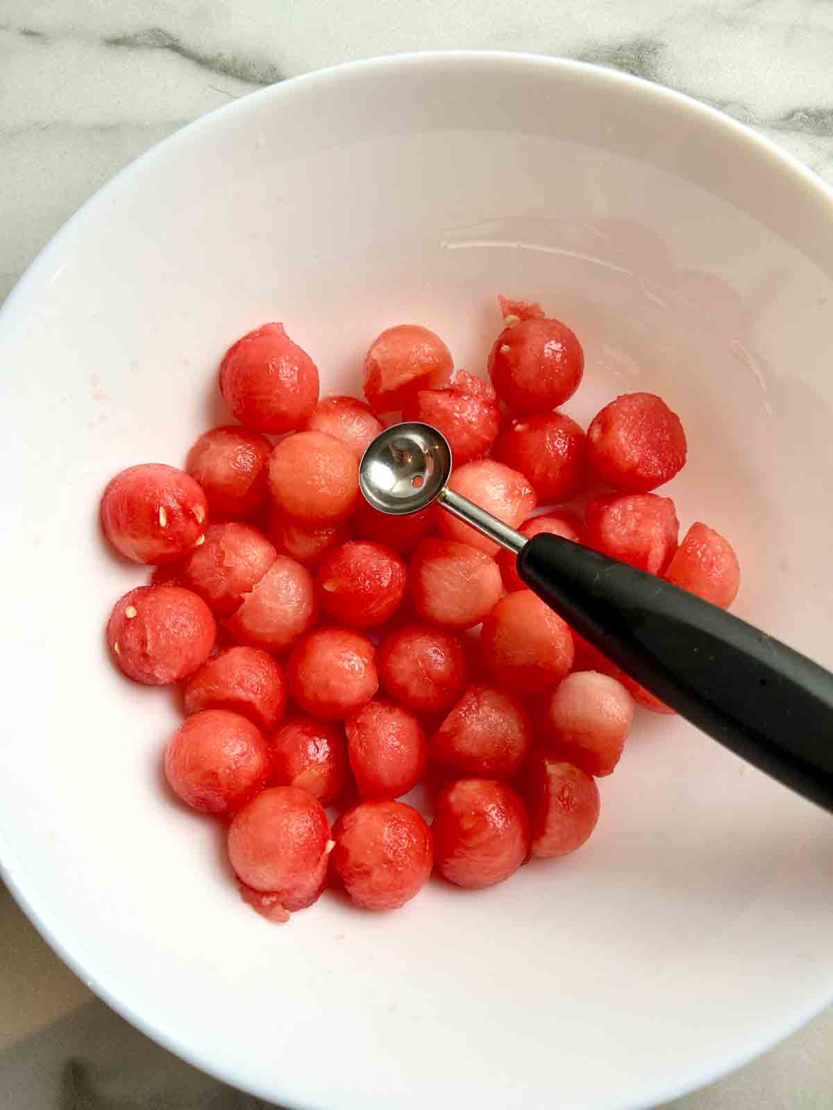 bowl of watermelon balls along with melon baller.