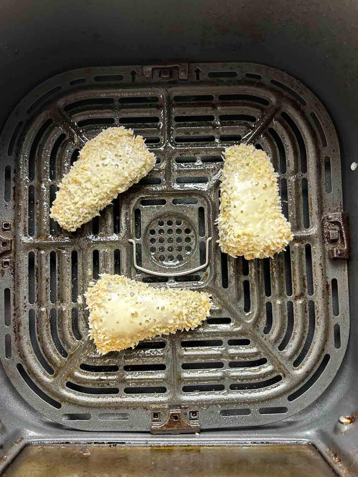 breaded sardines with oil sprayed on them, arranged in air-fryer basket.