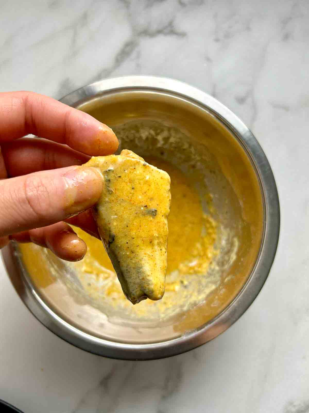 hand holding sardine covered in egg wash.