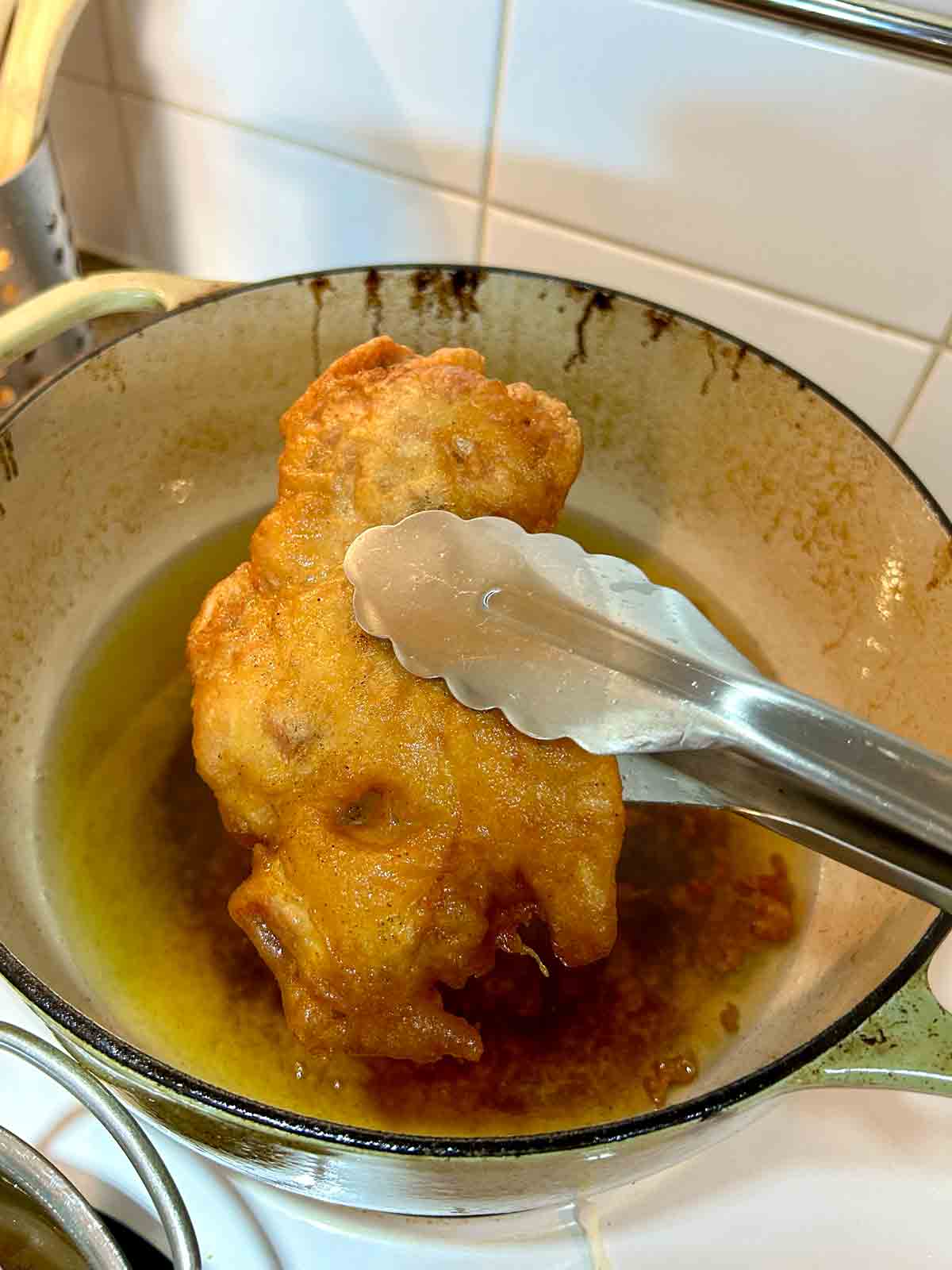 piece of fried chicken being pulled out of oil with tongs.