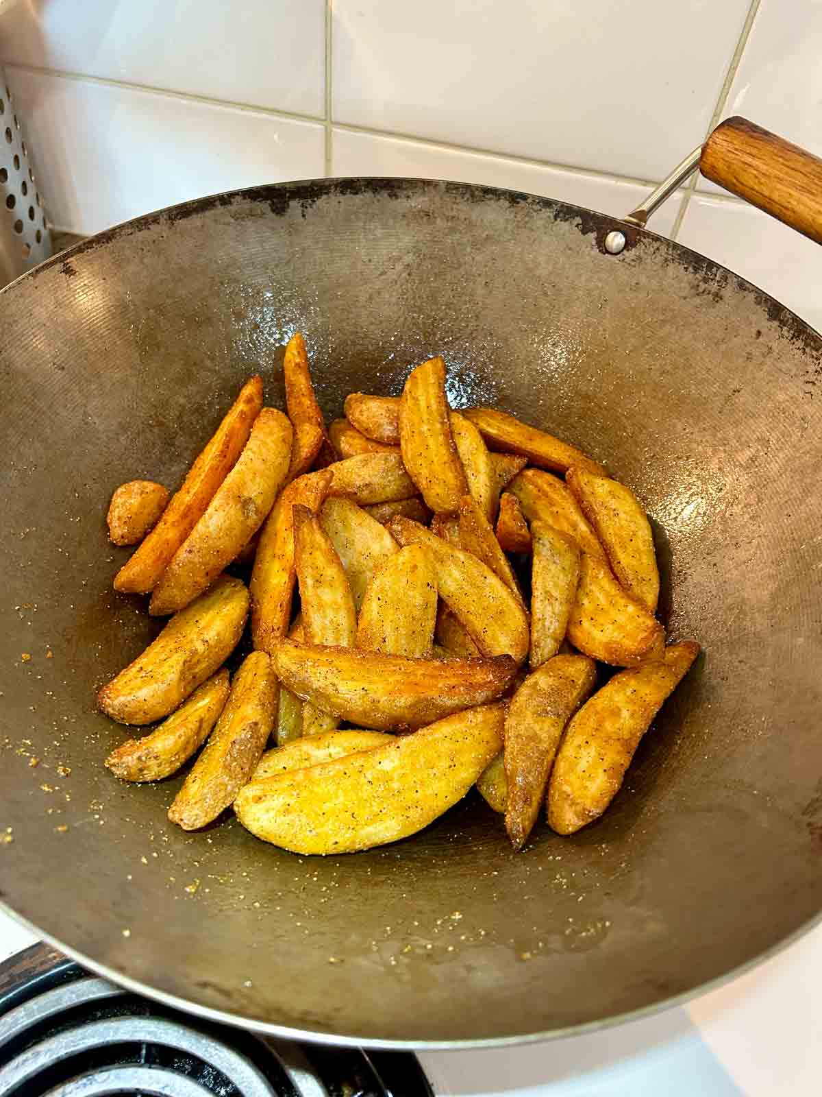 potato wedges being tossed with butter in wok.