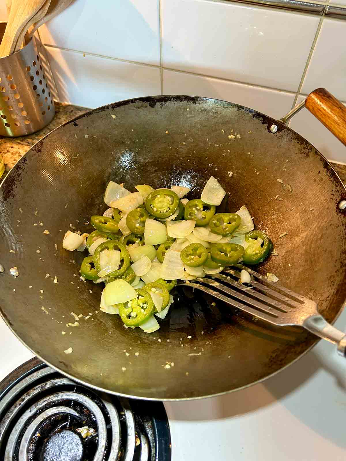 onions, garlic, and jalapenos being cooked in wok.