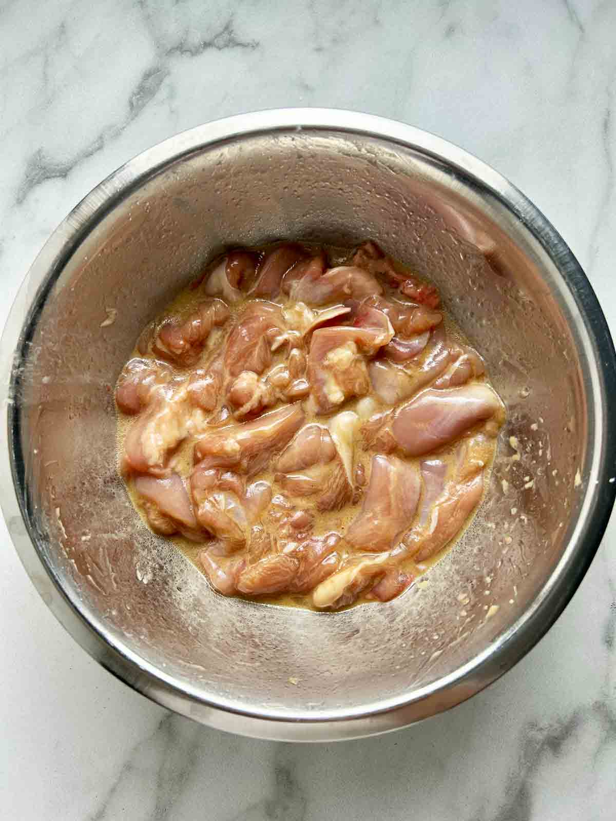 chicken pieces being marinated in bowl.