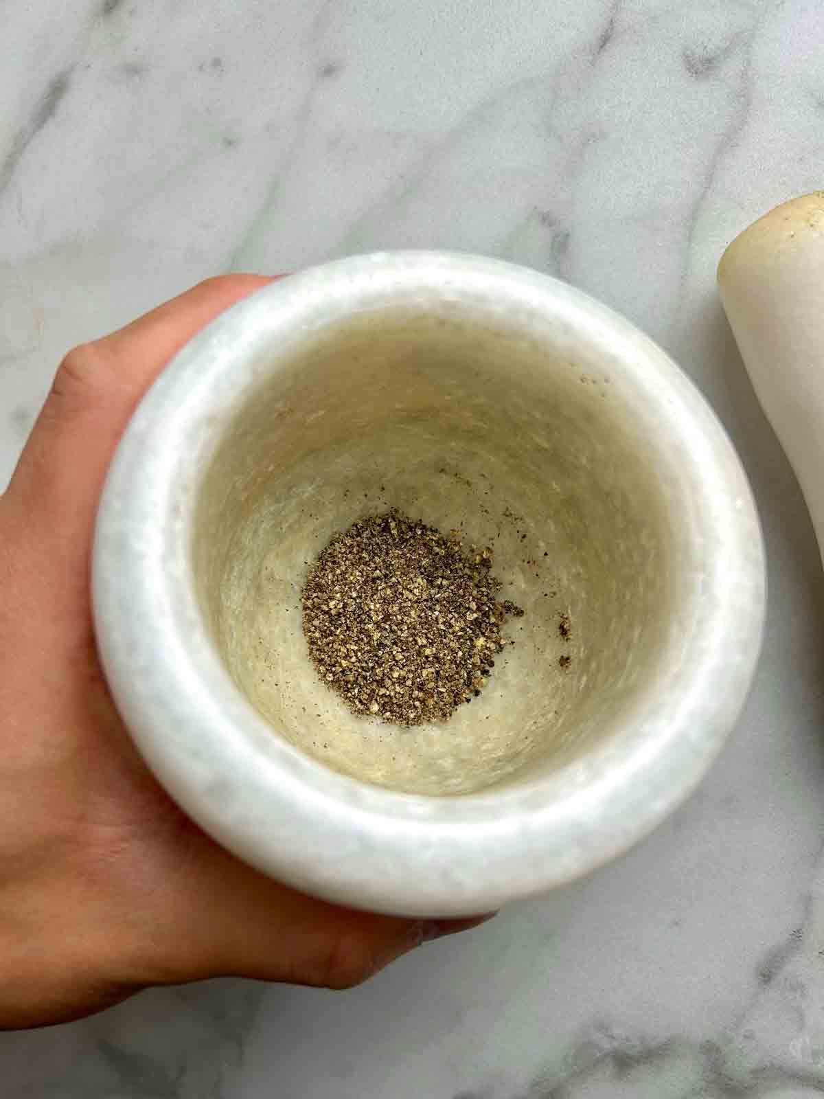 black pepper being pounded into coarse granules in a mortar and pestle.