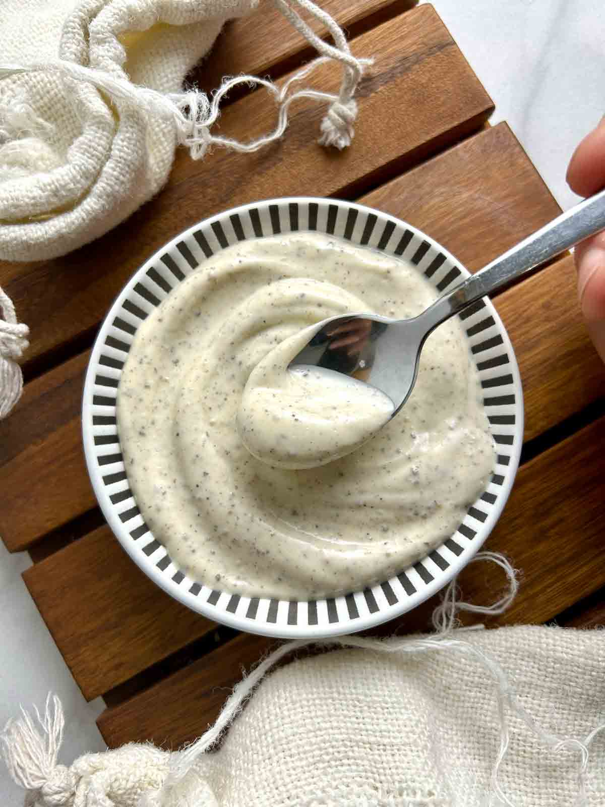 spoon lifting black pepper mayo from bowl of sauce.