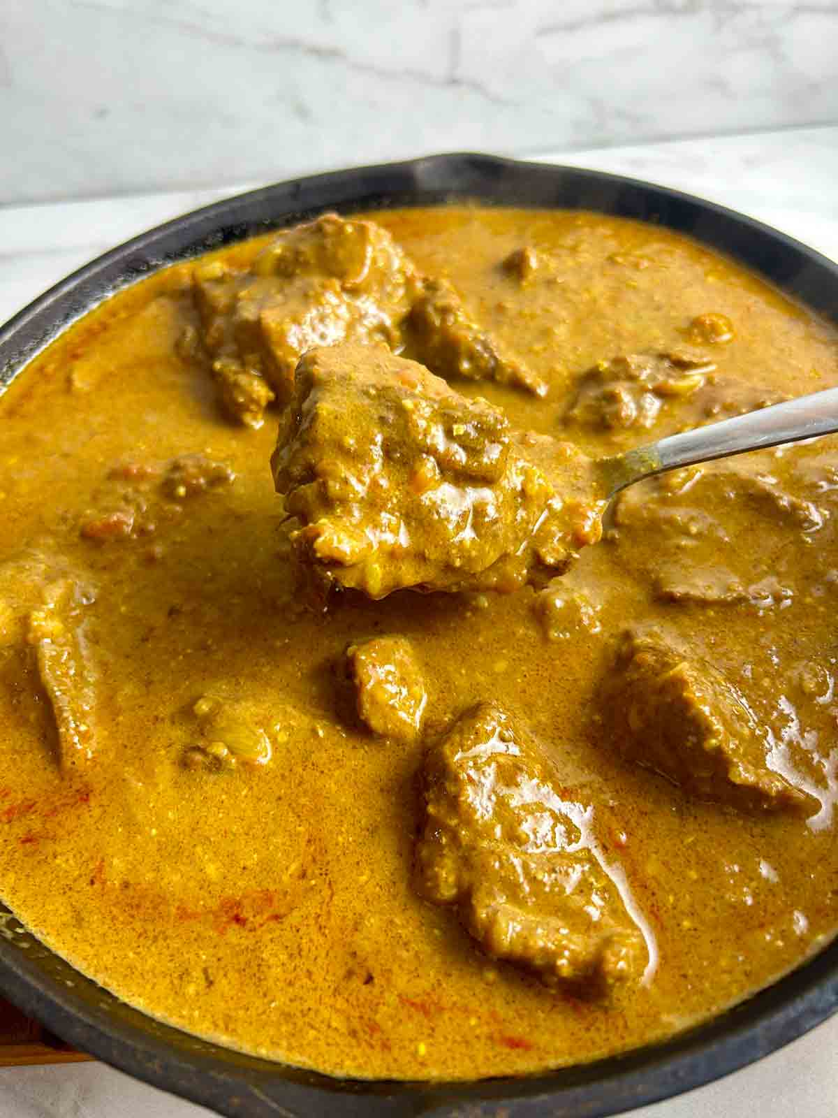 spoon lifting out piece of lamb from pan of curry.