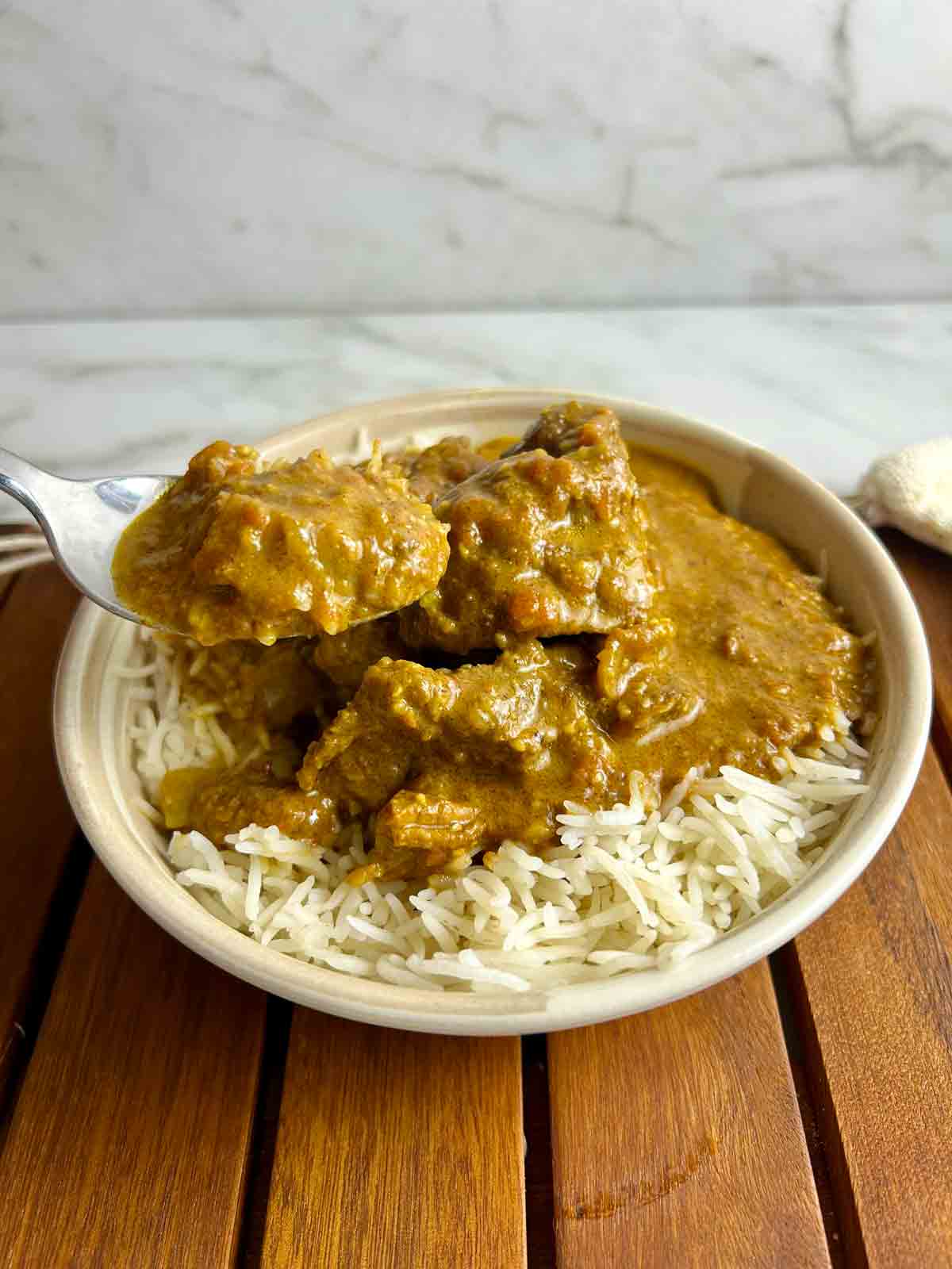 spoon lifting out lamb curry from bowl of rice.