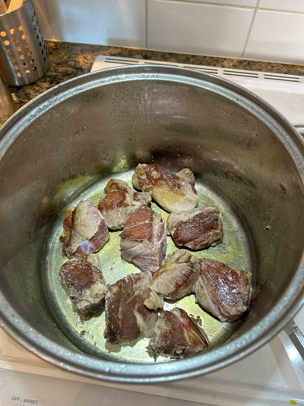 pieces of lamb meat being seared in pot.