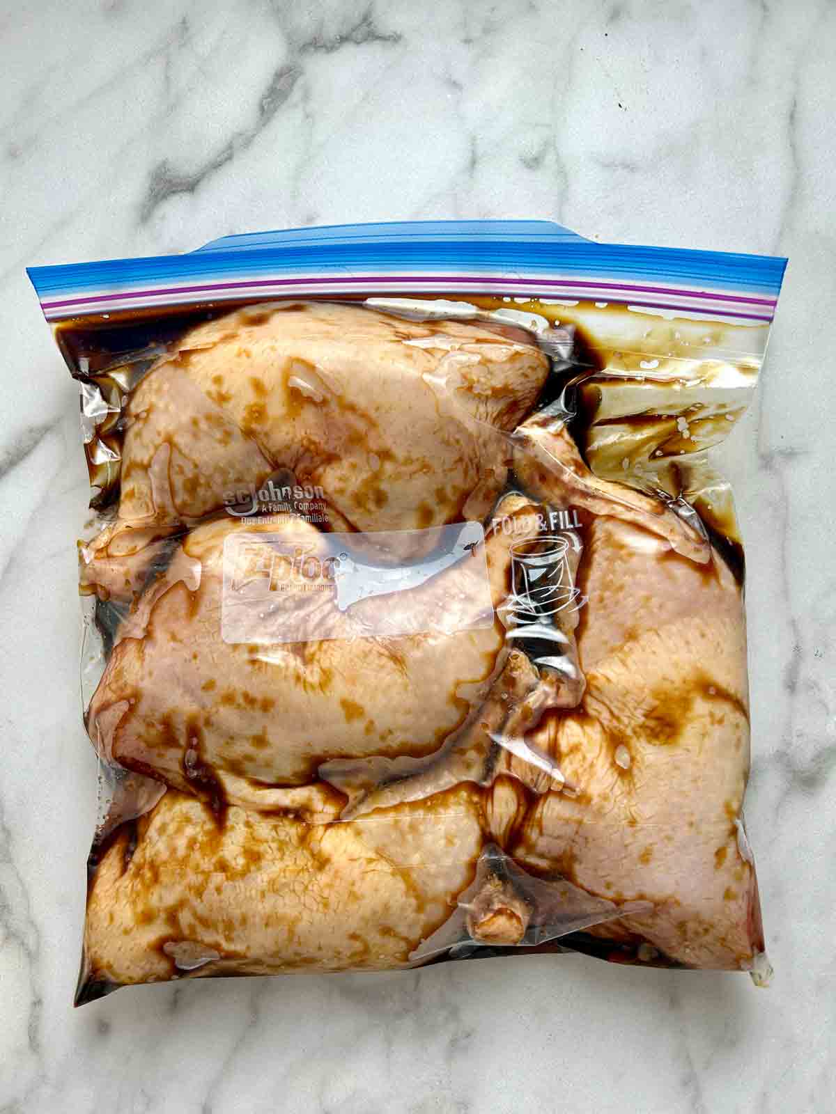 four chicken legs being marinated in plastic bag.