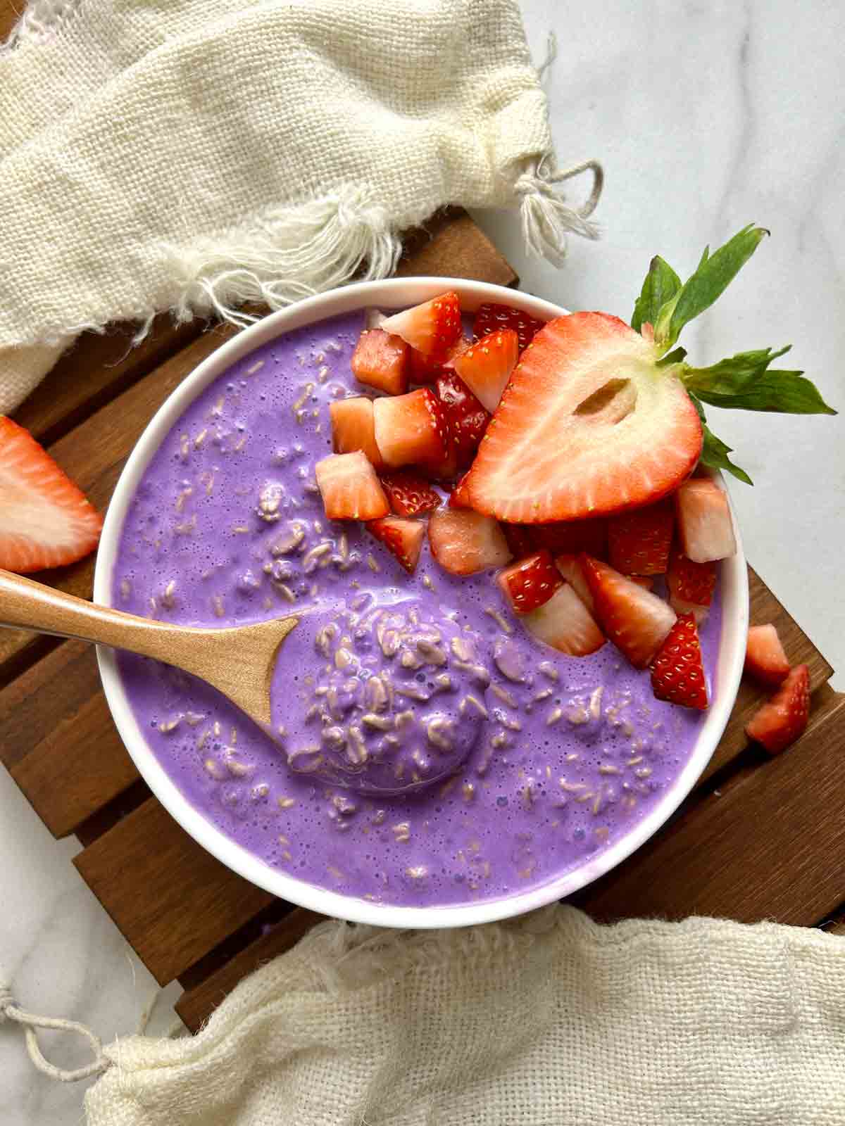 overhead shot of bowl of ube overnight oats with chopped strawberries.