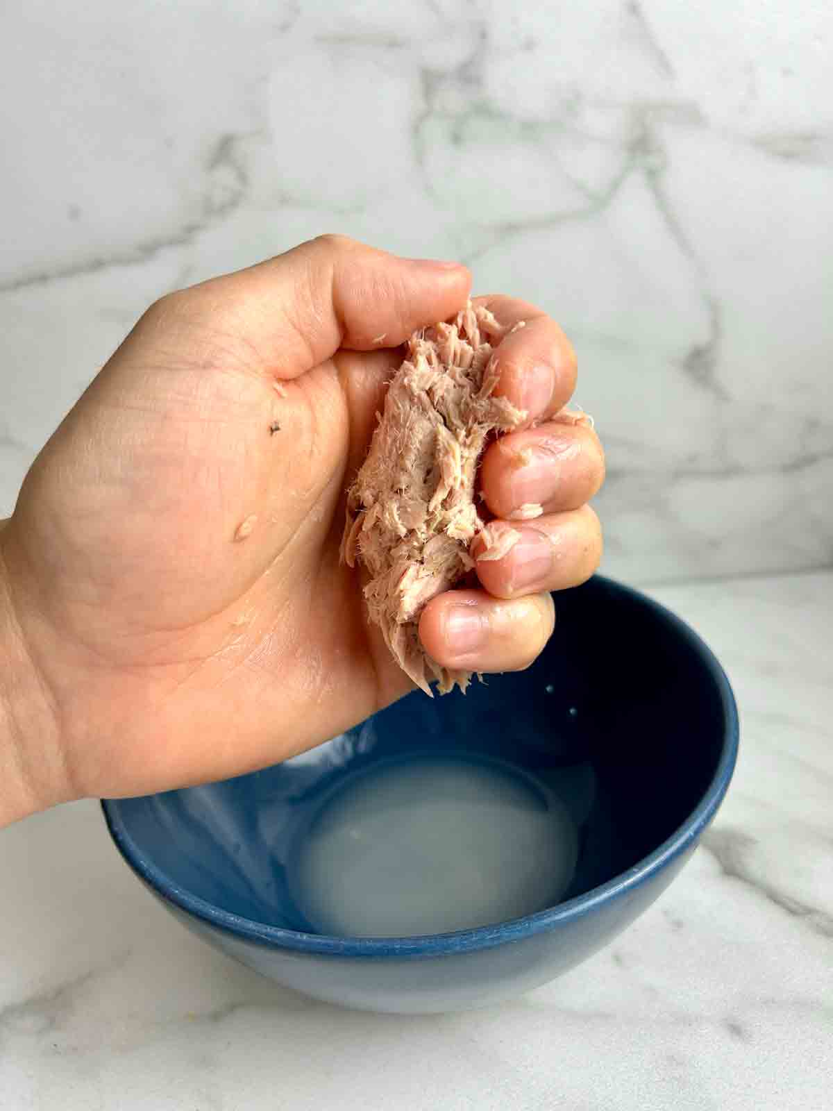 hand squeezing water from canned tuna.