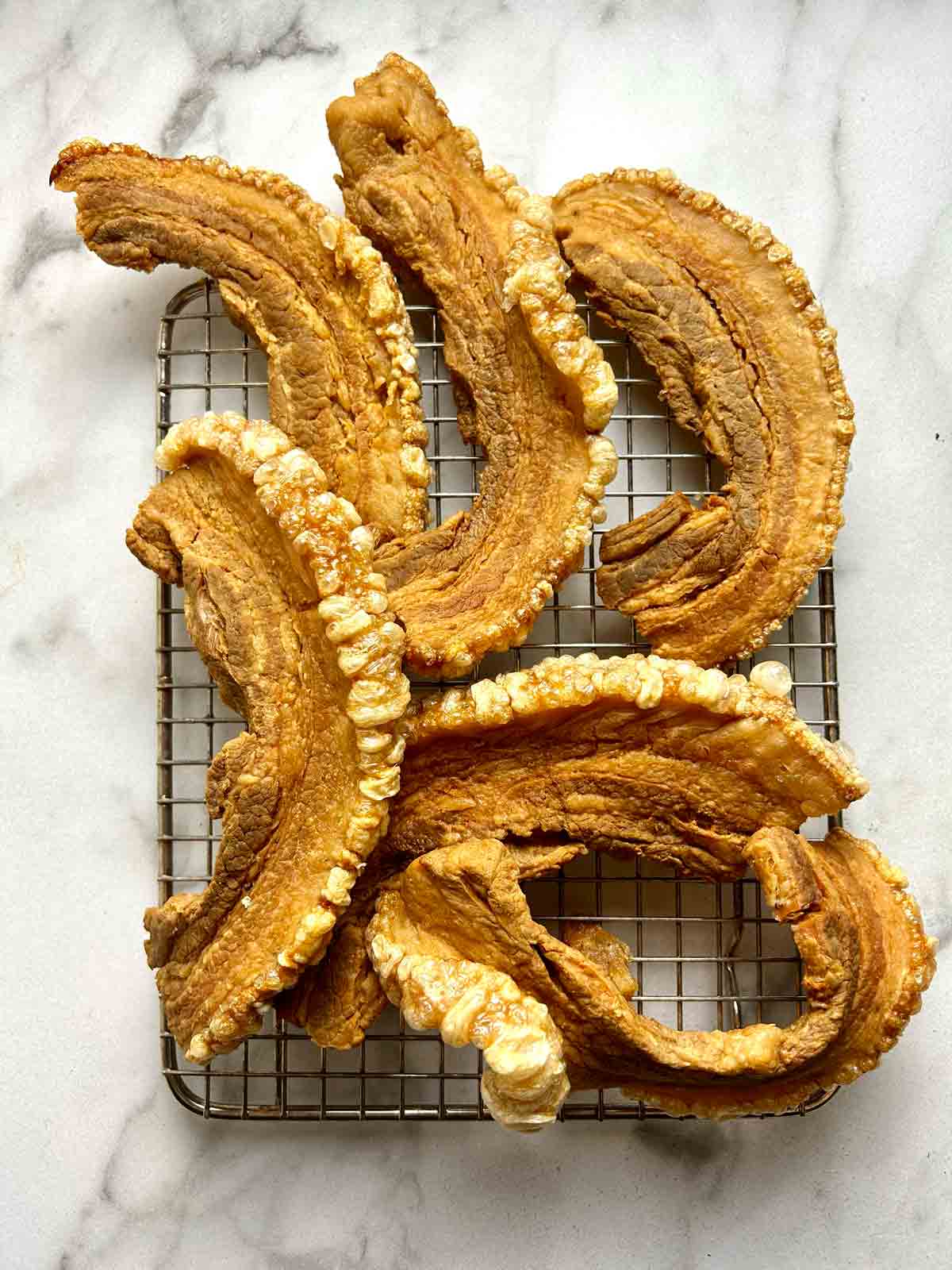 fried pork belly slices with puffed skin on wire rack.