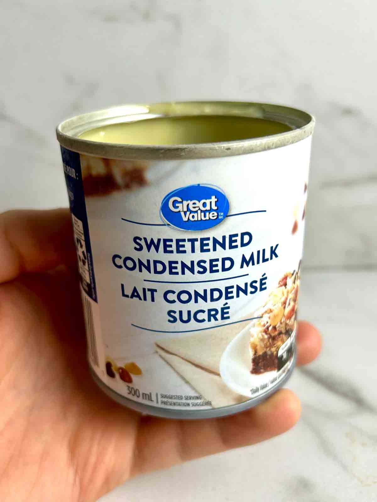 hand holding can of opened sweetened condensed milk.