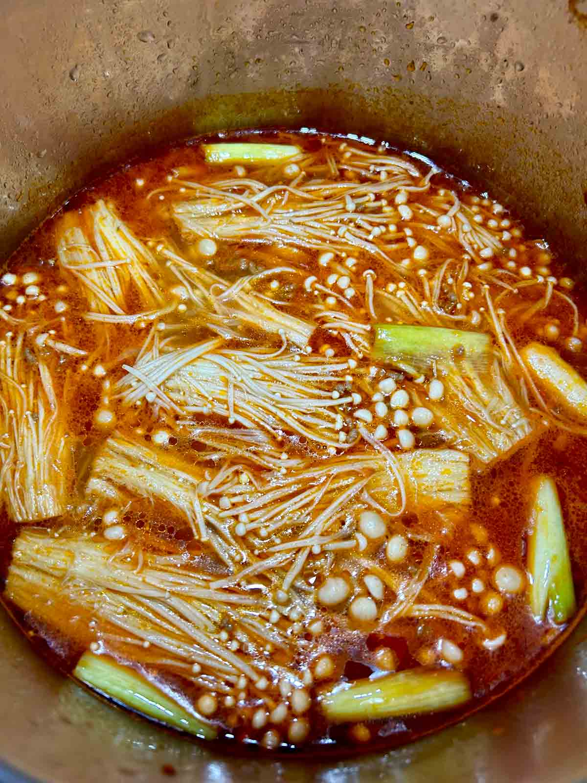 close up of enoki mushrooms simmering in soup pot.