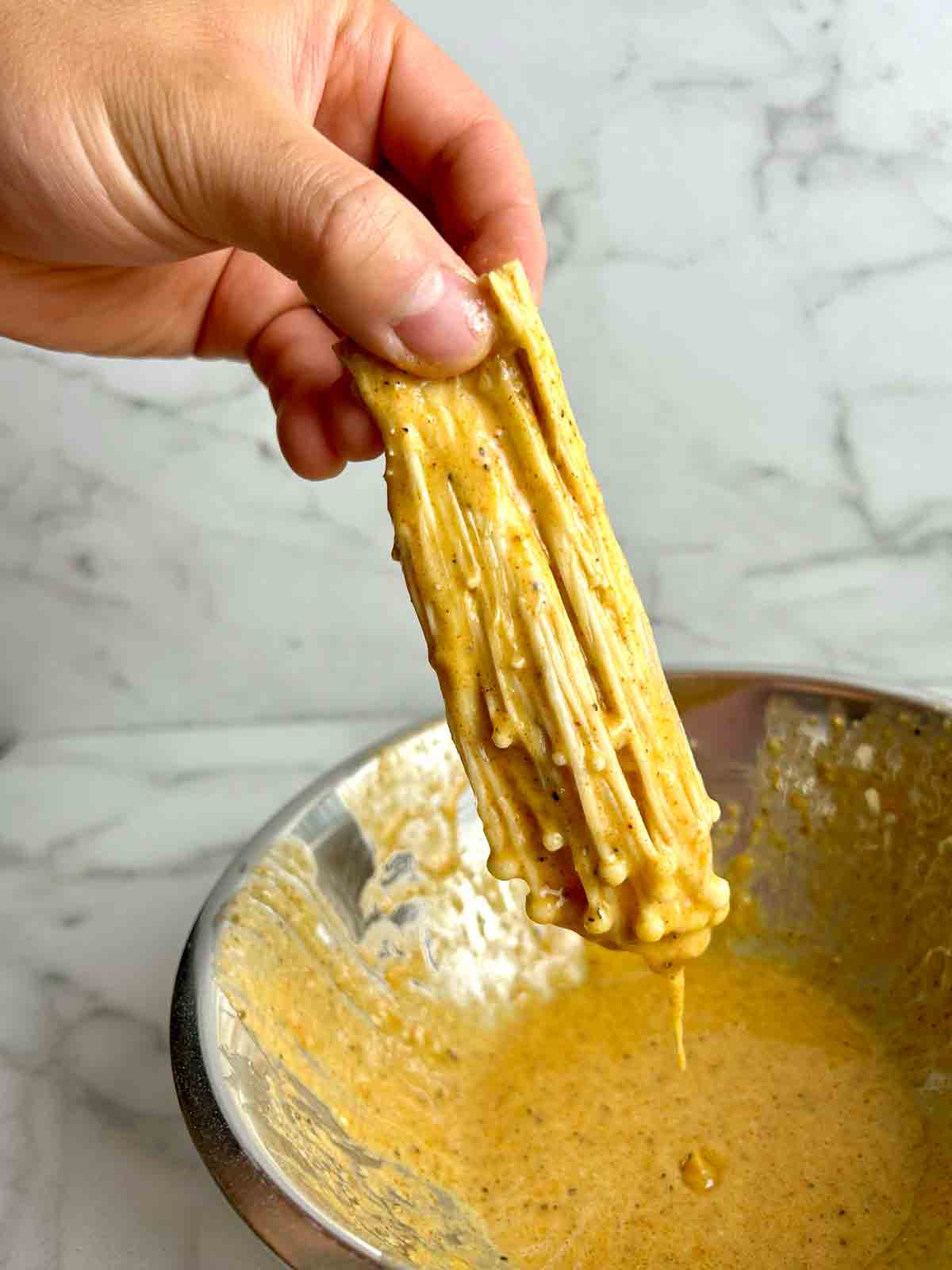 enoki mushroom being dipped in egg wash.