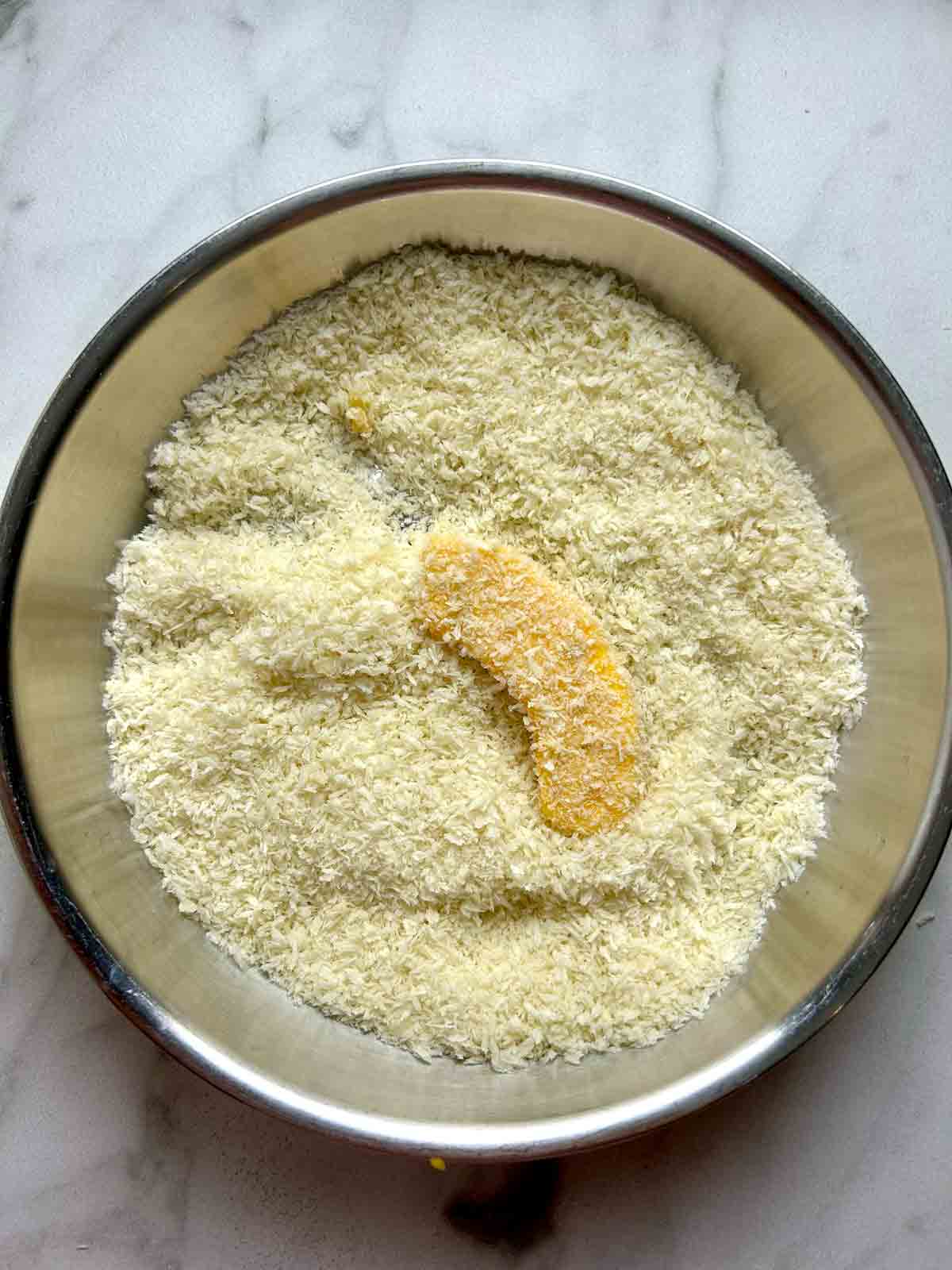 pumpkin slice being coated in dish of breadcrumbs.