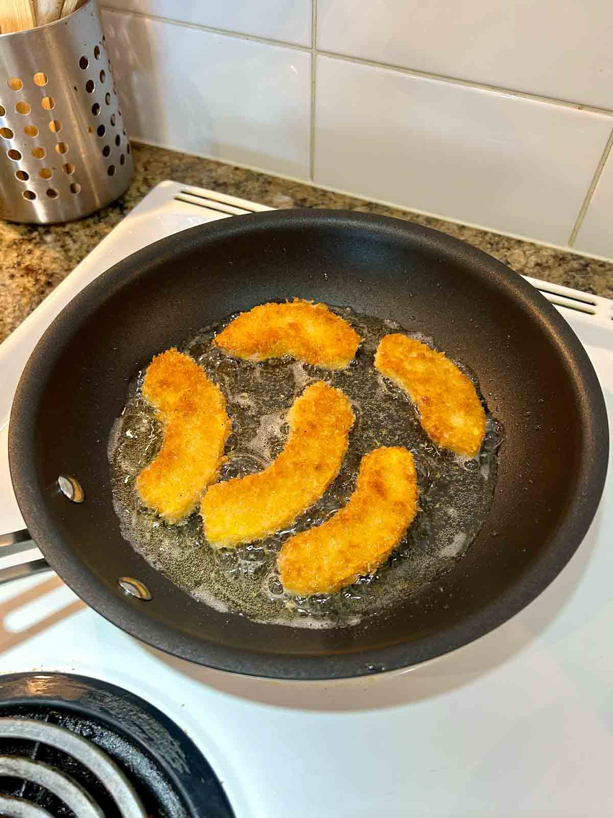 bread pumpkin slices being shallow fried in nonstick pan.