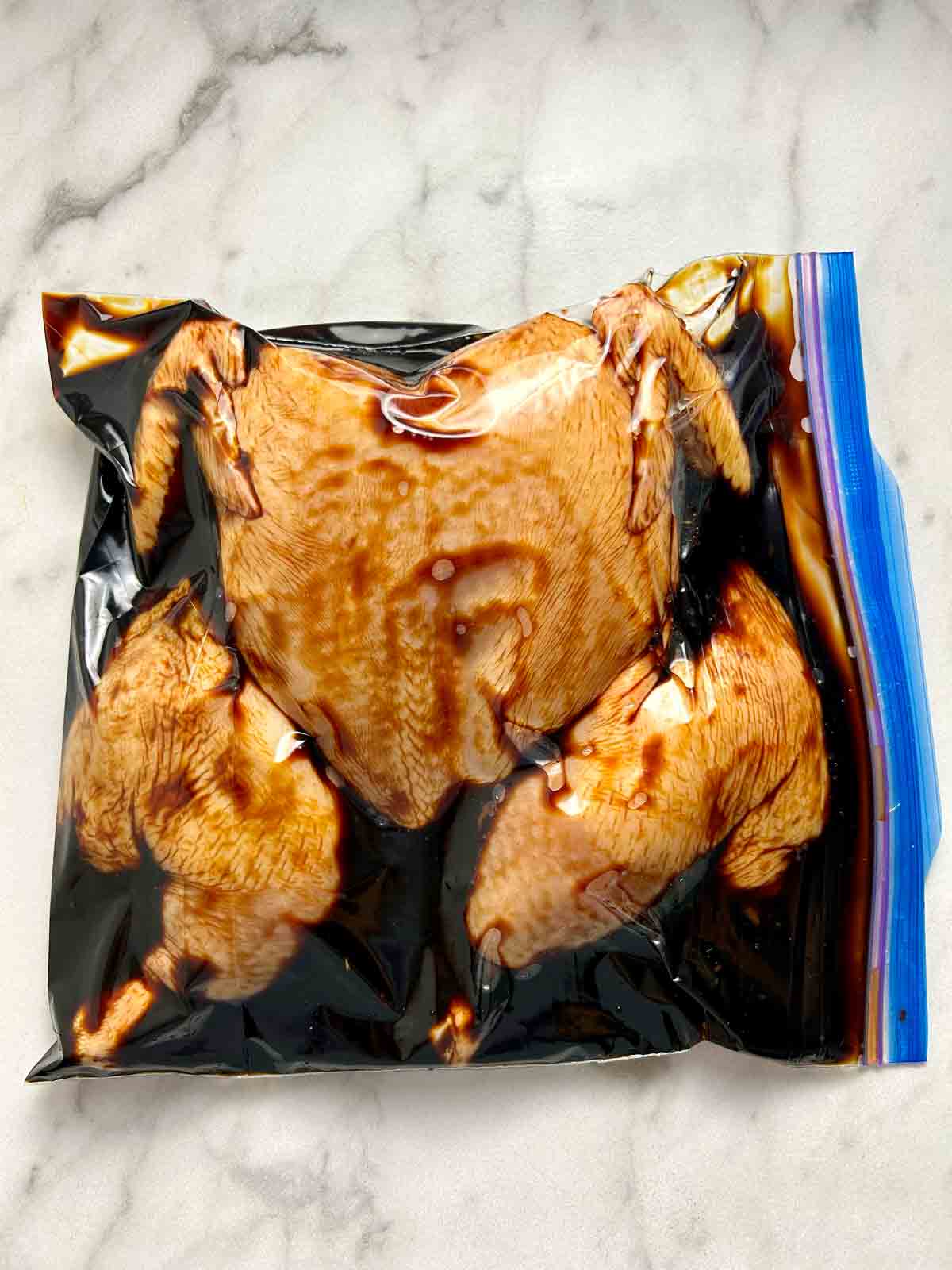 spatchcocked chicken being marinated in zipper lock bag.