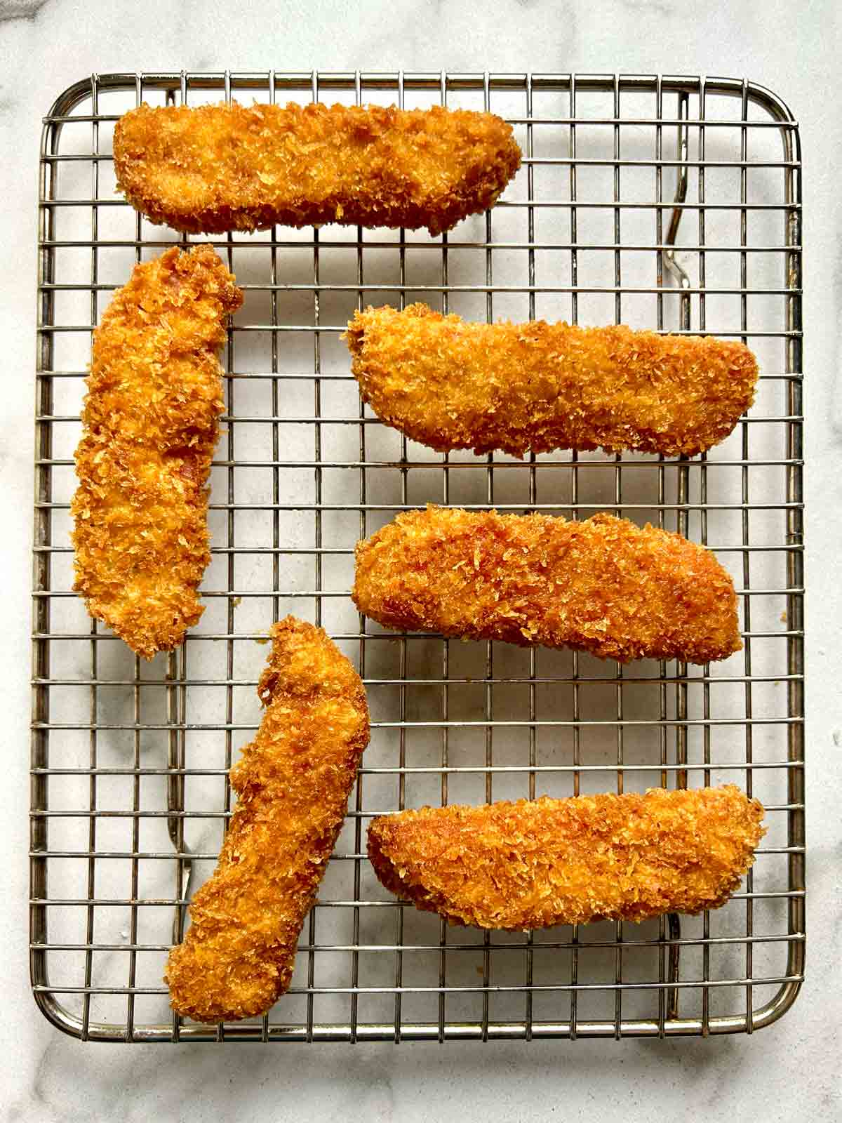 deep-fried Spam sticks drying on wire rack.