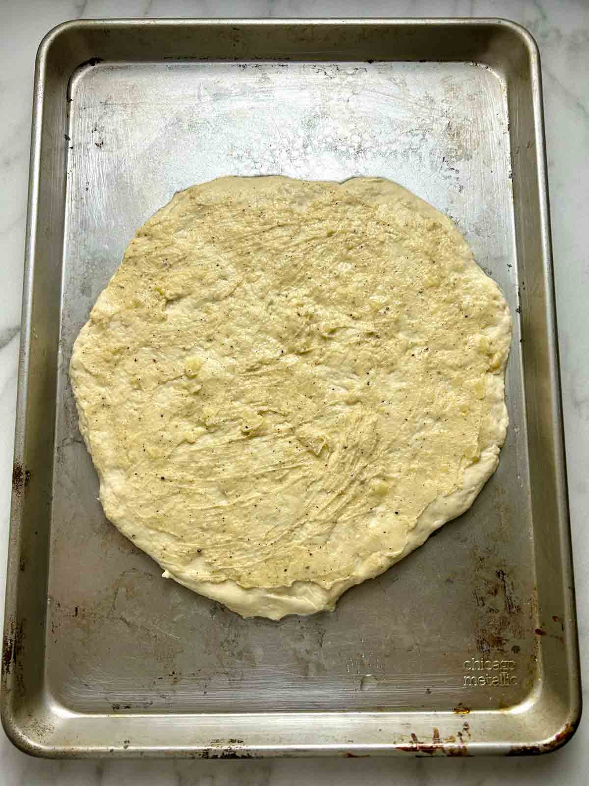 dough shaped into circle on pizza pan with garlic butter spread on.