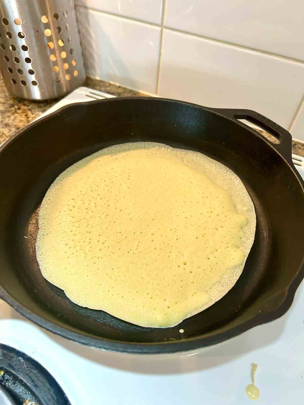 first side of crepe being cooked in cast iron pan.