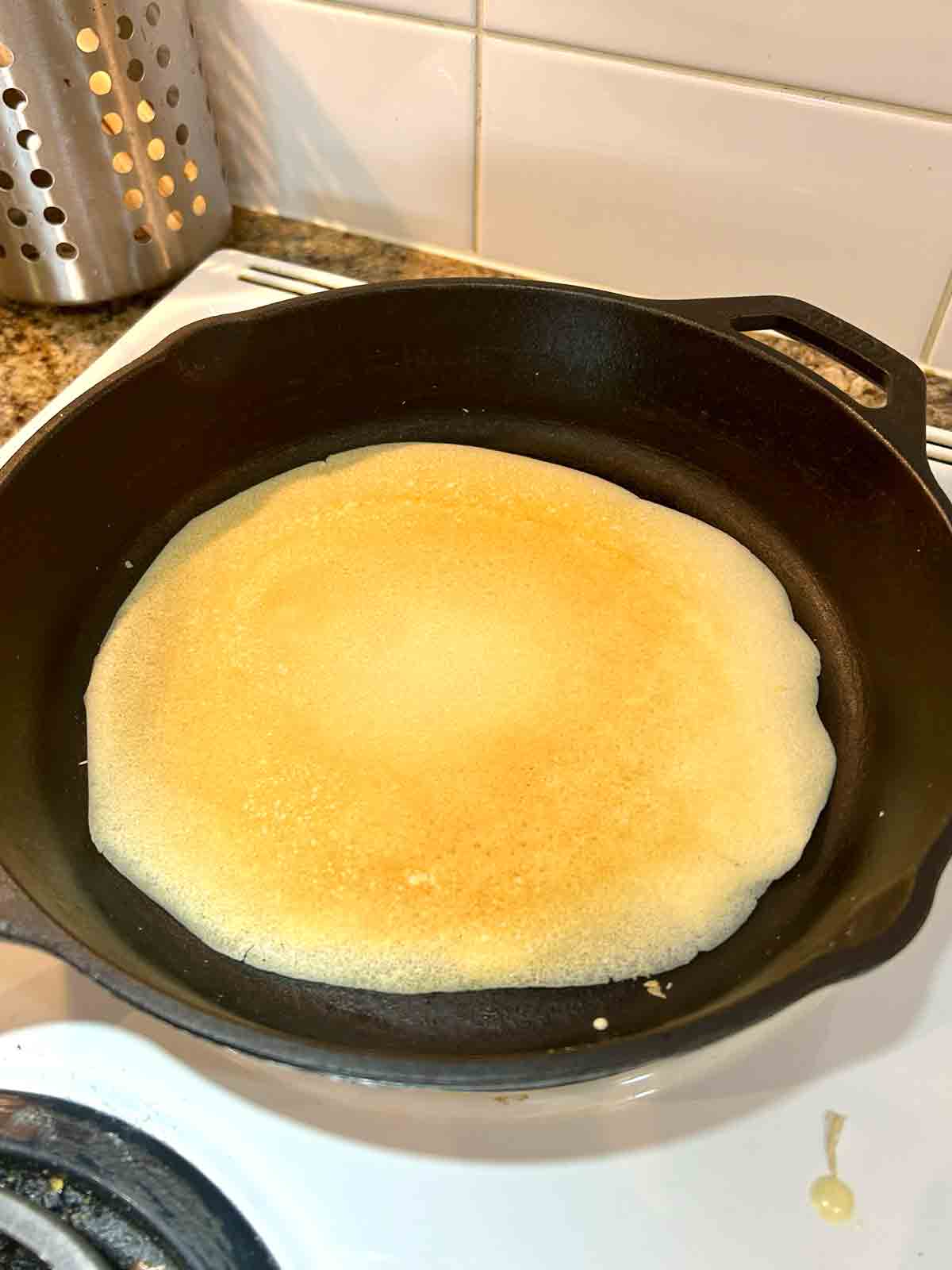 second side of crepe being cooked in cast iron pan.