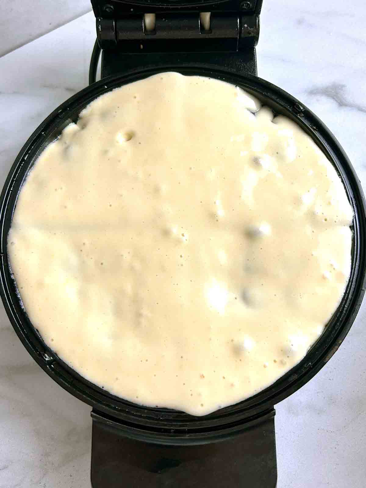 batter being spread into the bottom of the waffle iron.