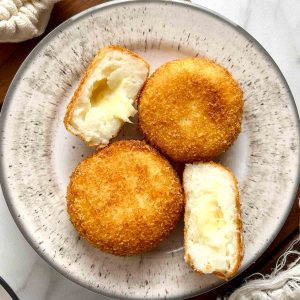 cheese croquettes on plate; one is cut in half to show cheese oozing out.