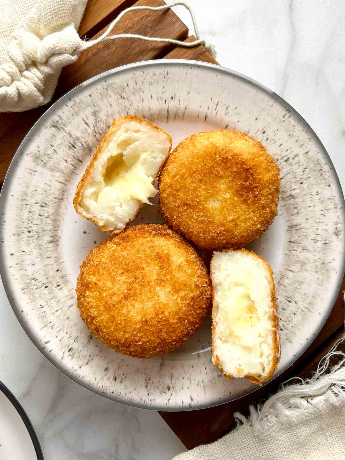 cheese croquettes on plate; one is cut in half to show cheese oozing out.