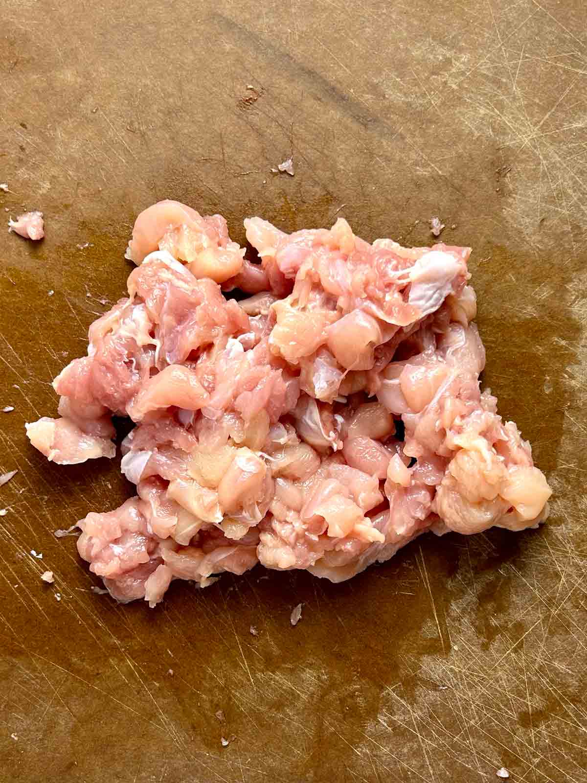 chicken drumstick meat being chopped into small pieces.