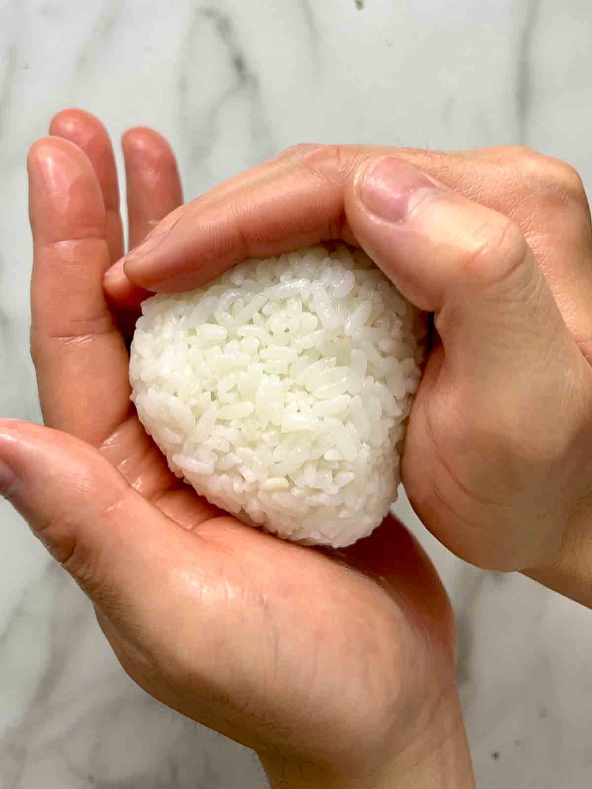 using hands to shape rice ball into triangle.