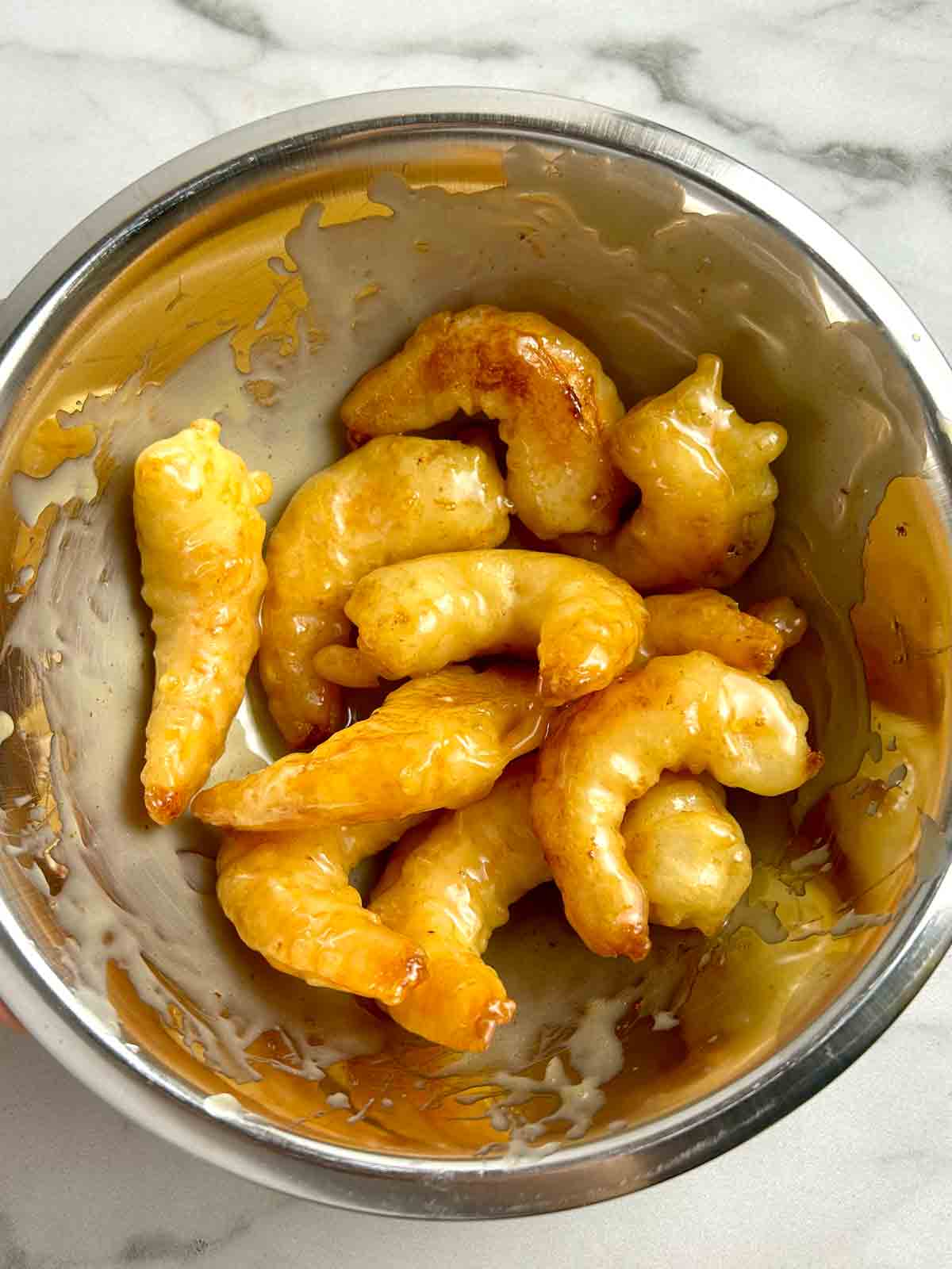 battered shrimp being tossed with sauce in bowl.