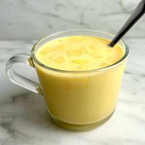 cup of mango milk with chopped mangoes on top.