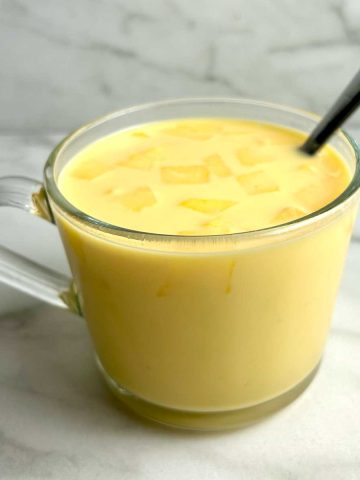 cup of mango milk with chopped mangoes on top.