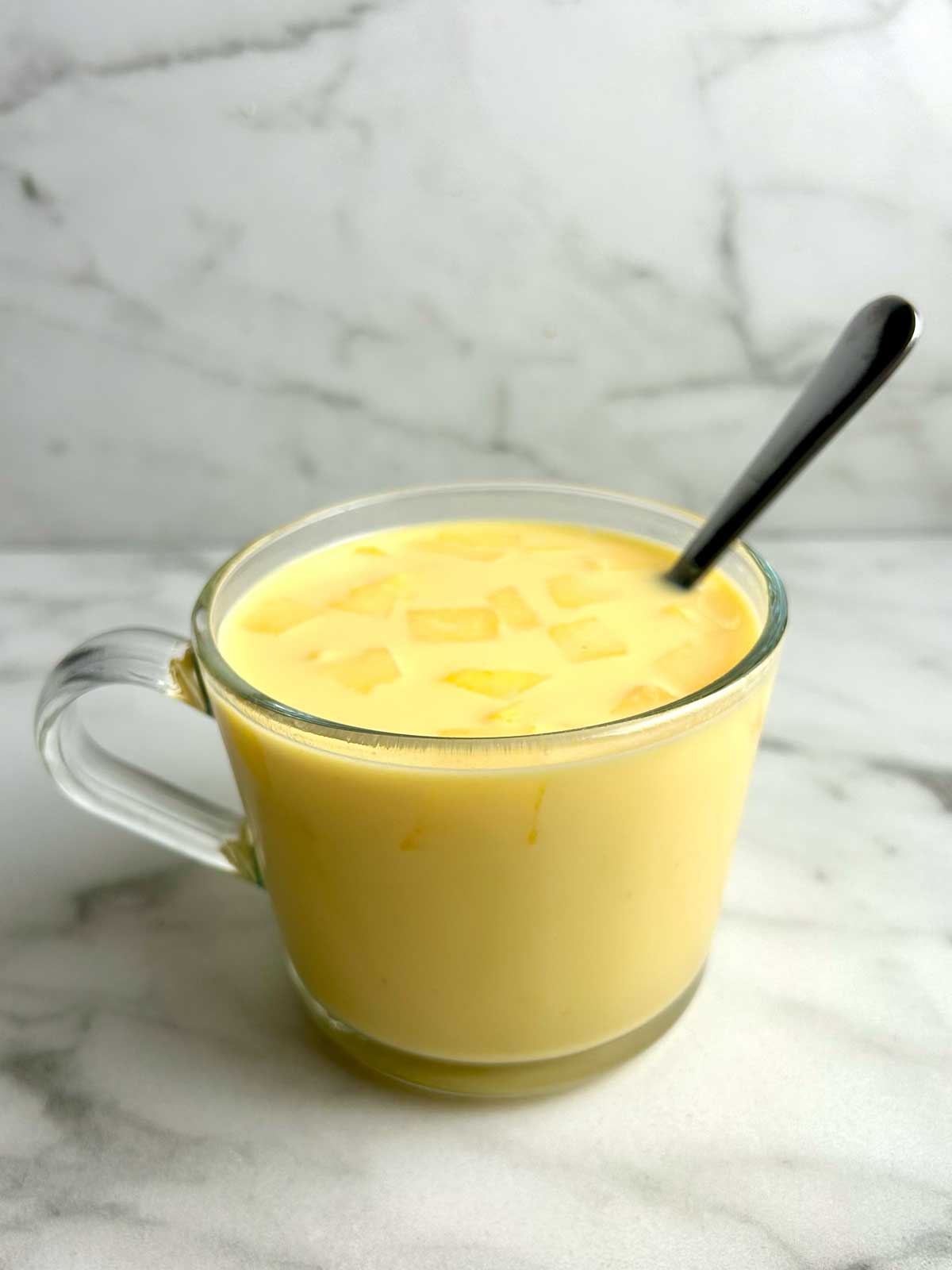 cup of mango milk with chopped mangoes on top.