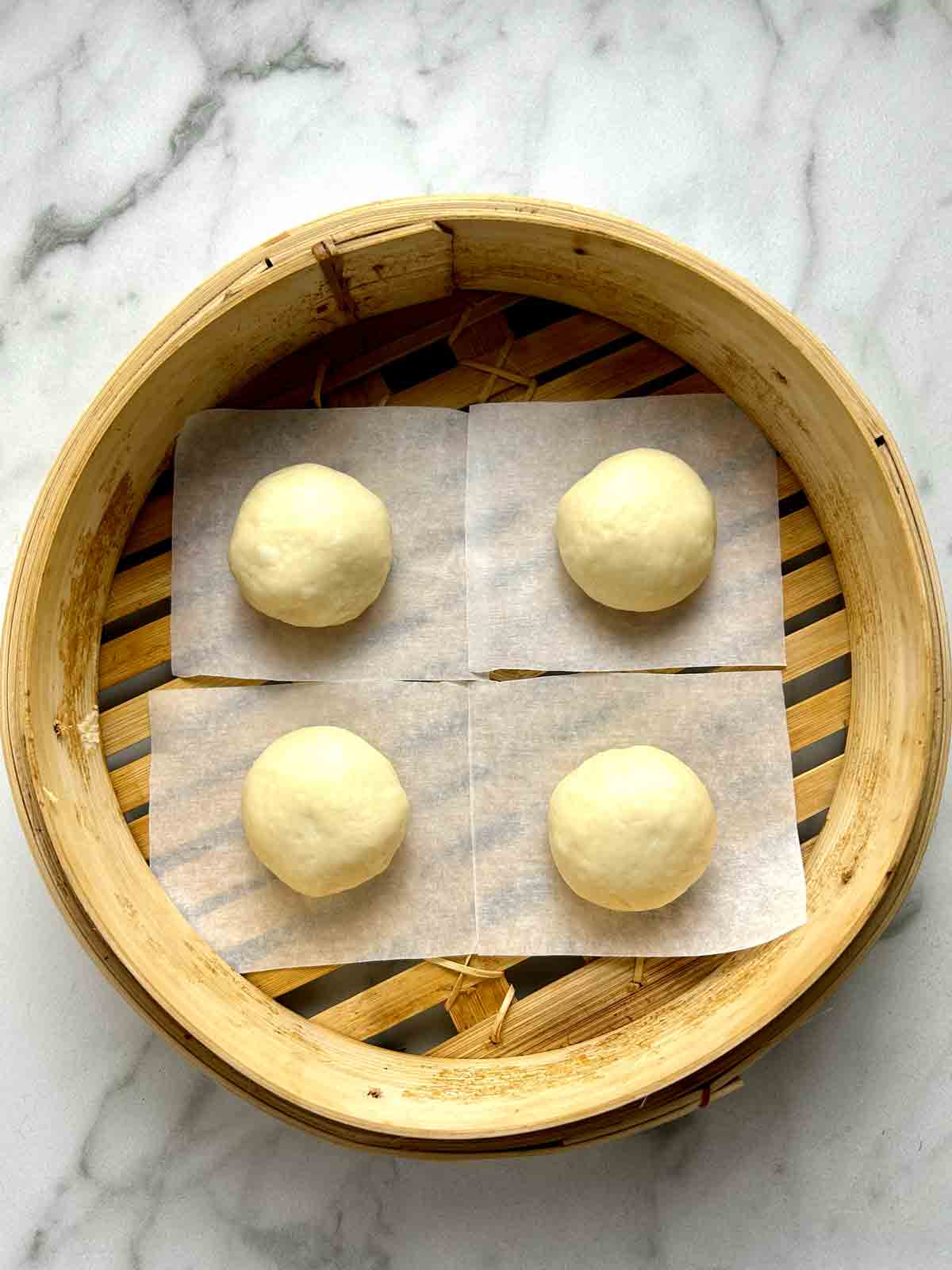 four dough balls in bamboo steamer before second proof.