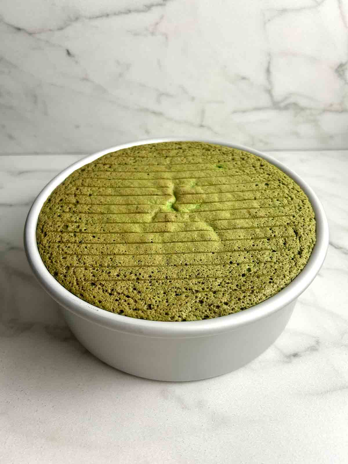 baked pandan cake cooling down in cake pan. there are small indents from the wire rack on the top of the cake.