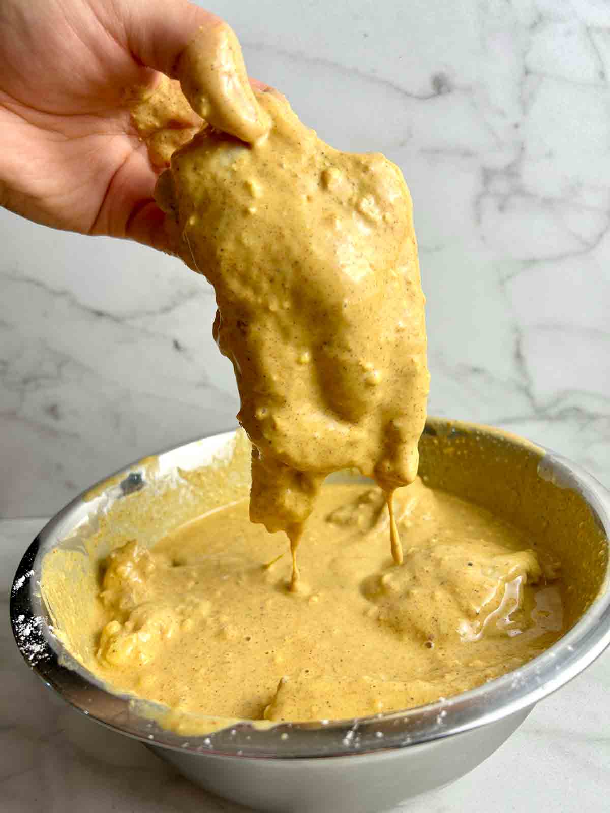 chicken being lifted out of buttermilk brine thickened with flour.