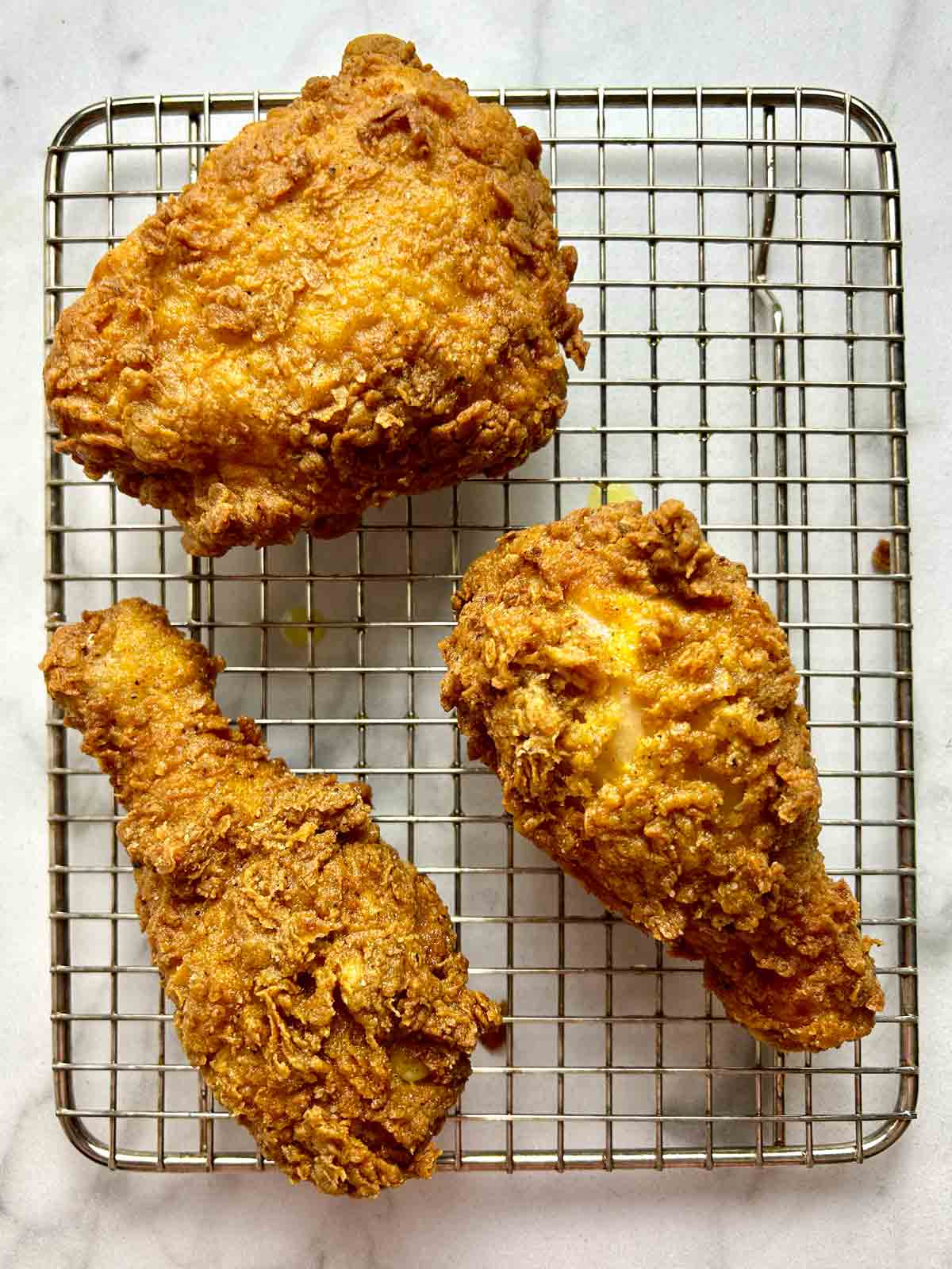 fried chicken pieces drying on wire rack.