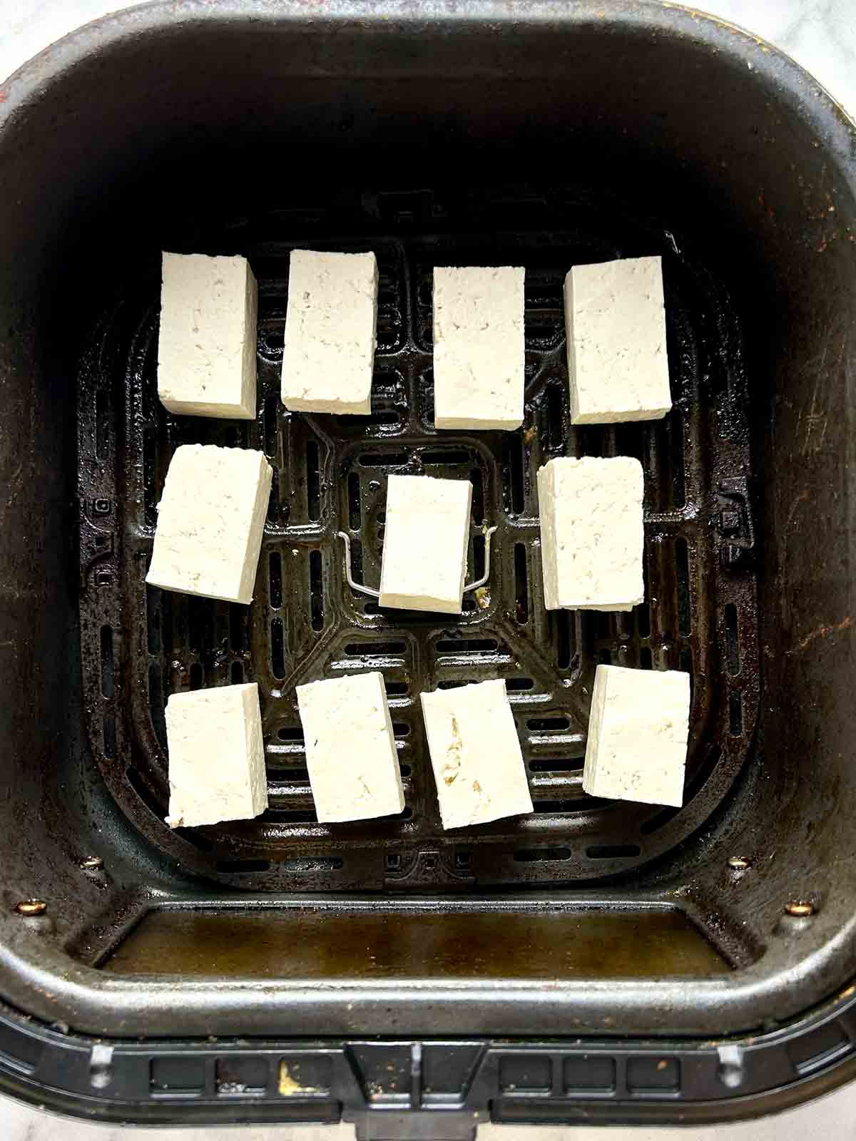 raw tofu pieces in air fryer basket.