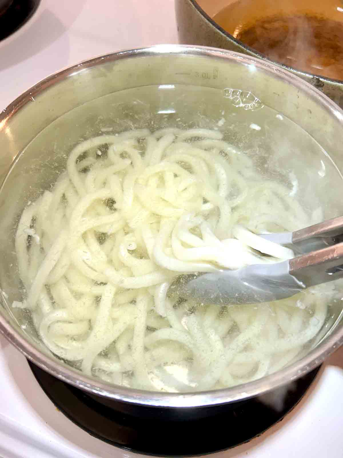 udon noodles being boiled in pot of water.