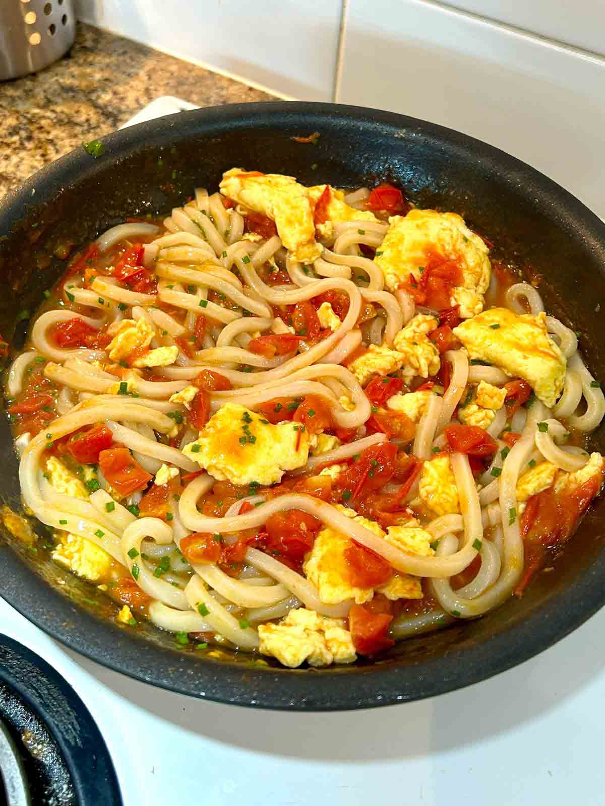 udon and chives mixed with tomato sauce and eggs in pan.