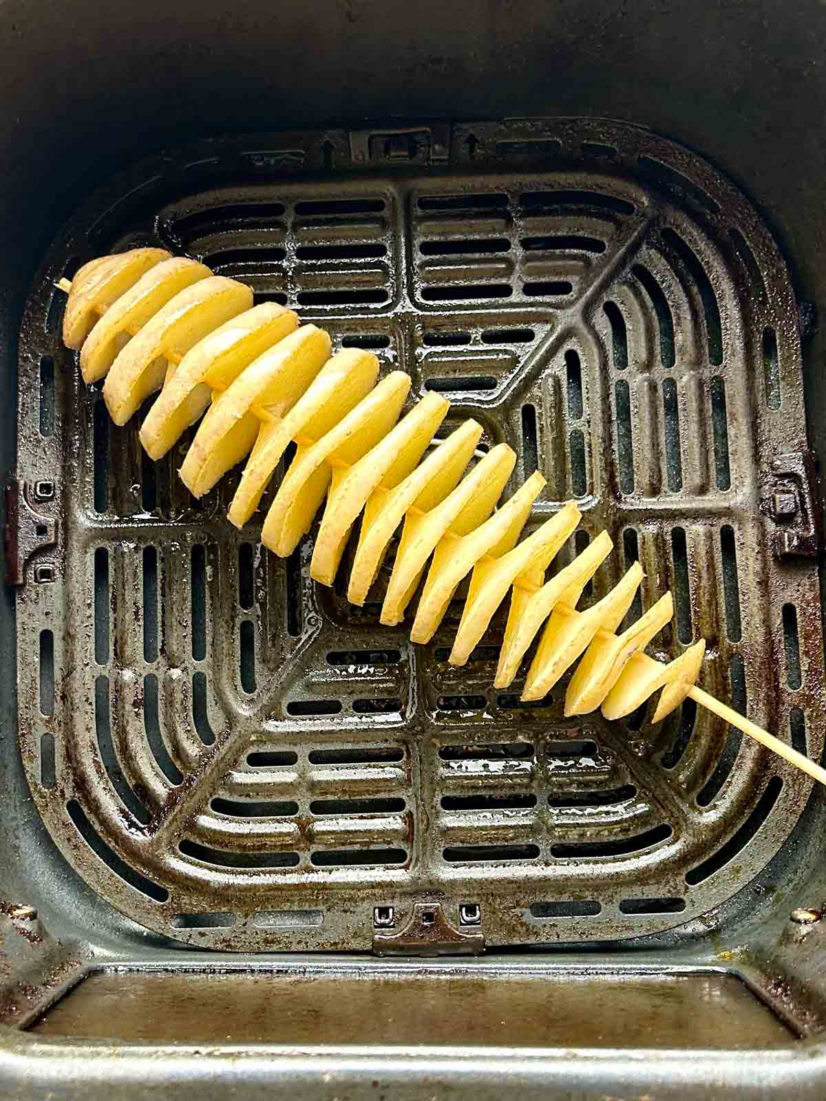 uncooked potato spiral in air fryer basket.